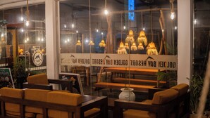 Et hyggeligt opholdsområde med møbler af træ og et stort vindue, der viser en skiltning til en restaurant.