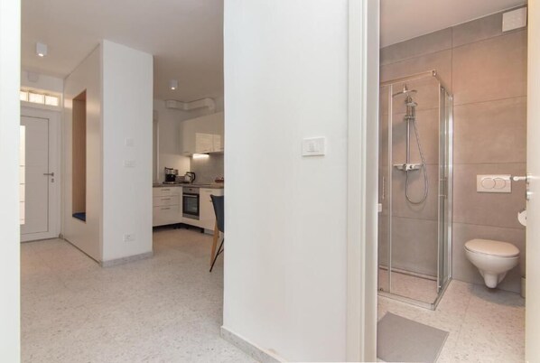 A modern apartment with a kitchen, a glass-enclosed shower, and a white toilet.