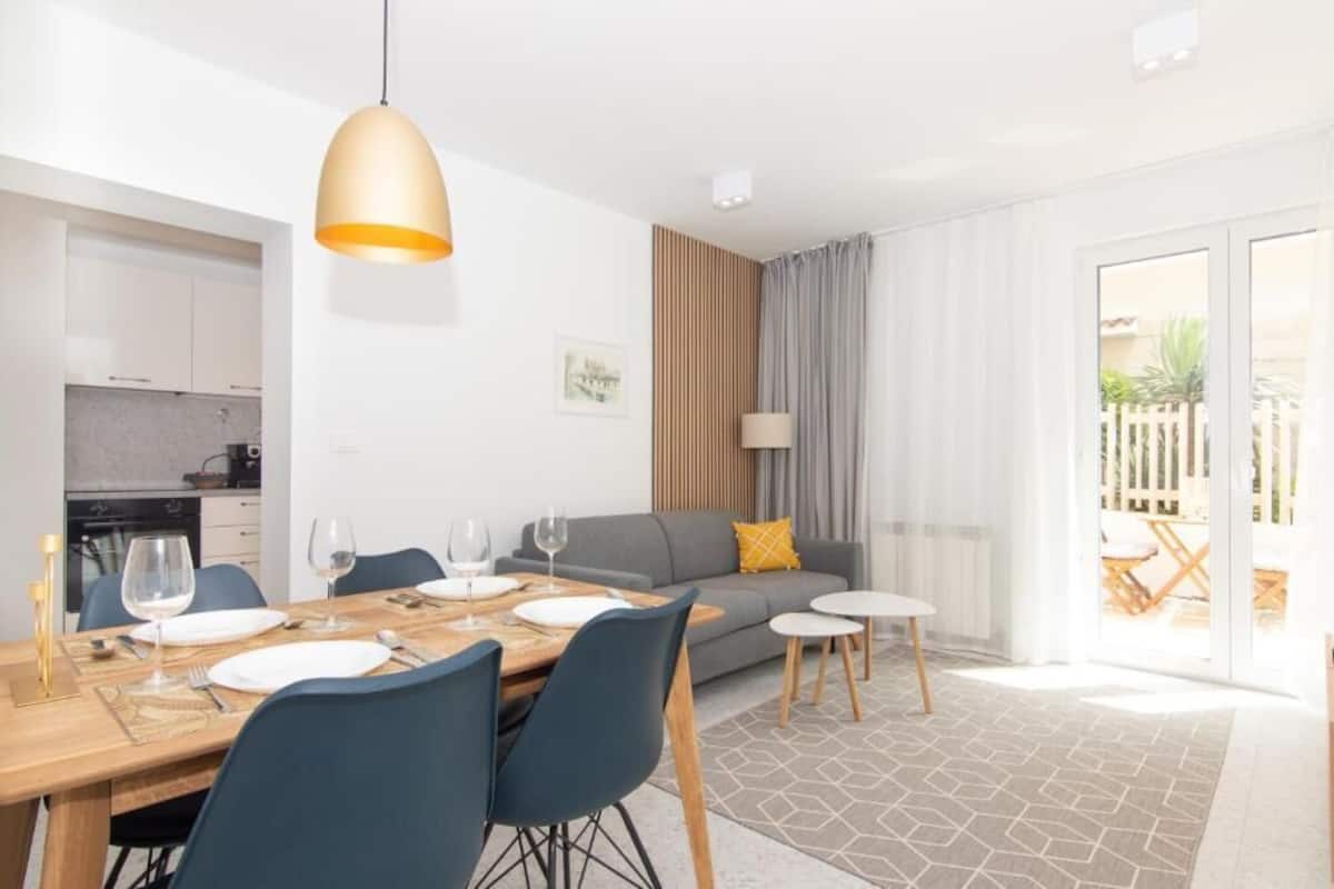 Una sala moderna con un sofá, una mesa de comedor para cuatro personas y una cocina al fondo.