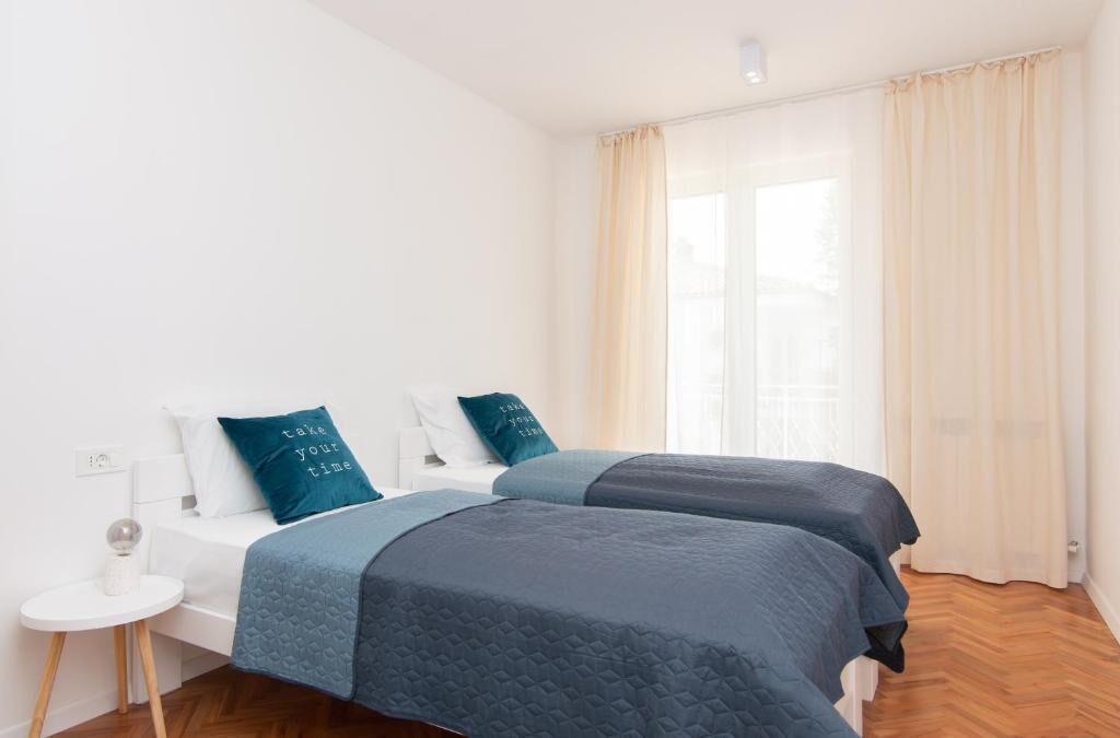 A modern bedroom with two beds, a small bedside table, and a large window with curtains.