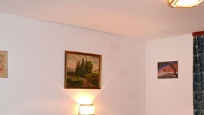 Una cama doble con ropa de cama blanca, dos mesitas de noche, una lámpara de pared y dos cuadros enmarcados.