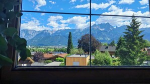 Una ventana con vistas a una cadena montañosa, un pueblo y un edificio con paneles solares.