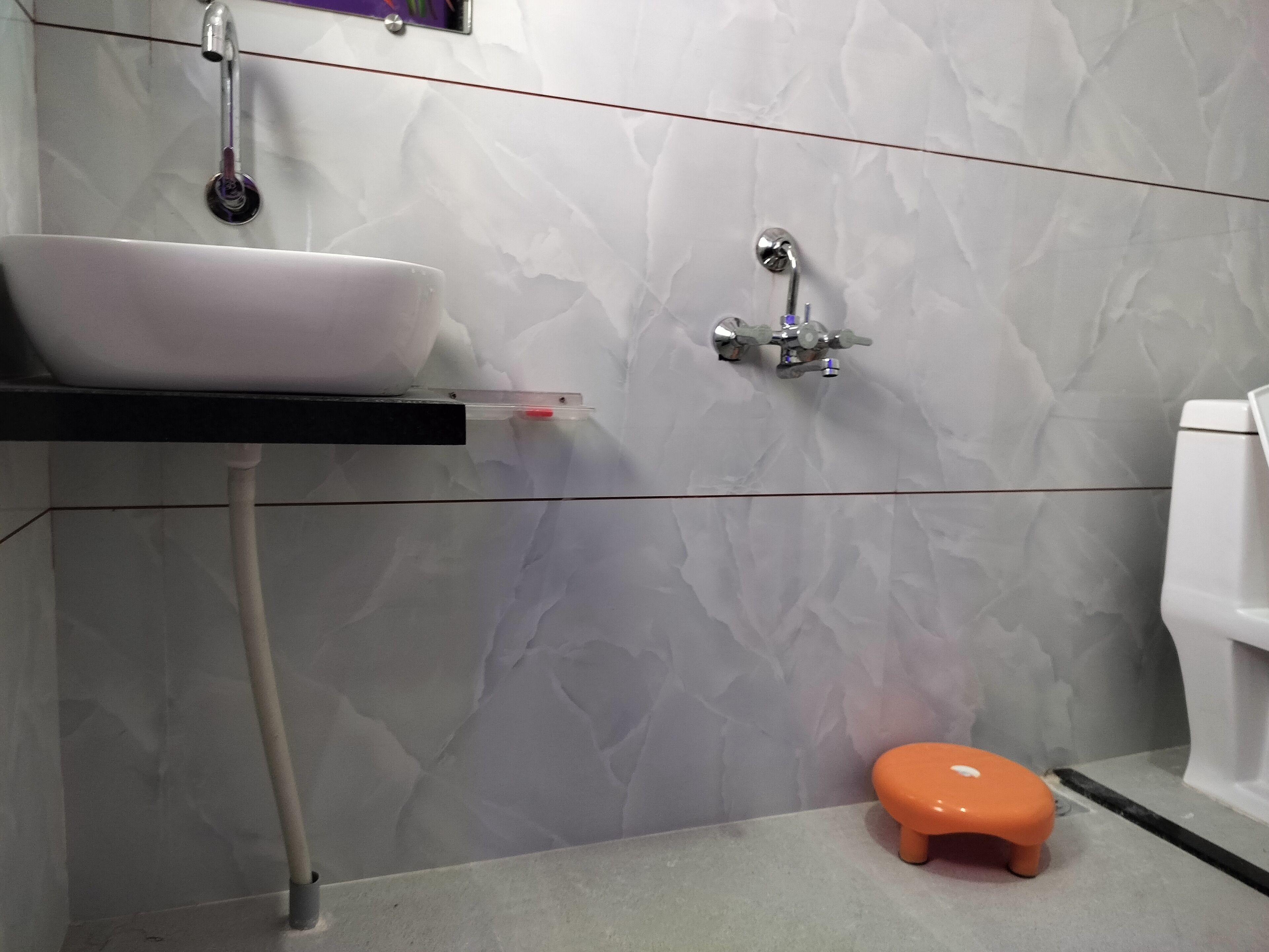 A bathroom with a white sink, a small orange stool, and a toilet.