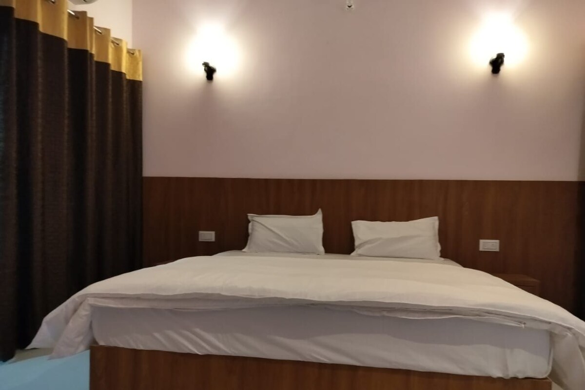 Un grand lit avec une tête de lit en bois, deux appliques murales et un rideau foncé sur le côté gauche.