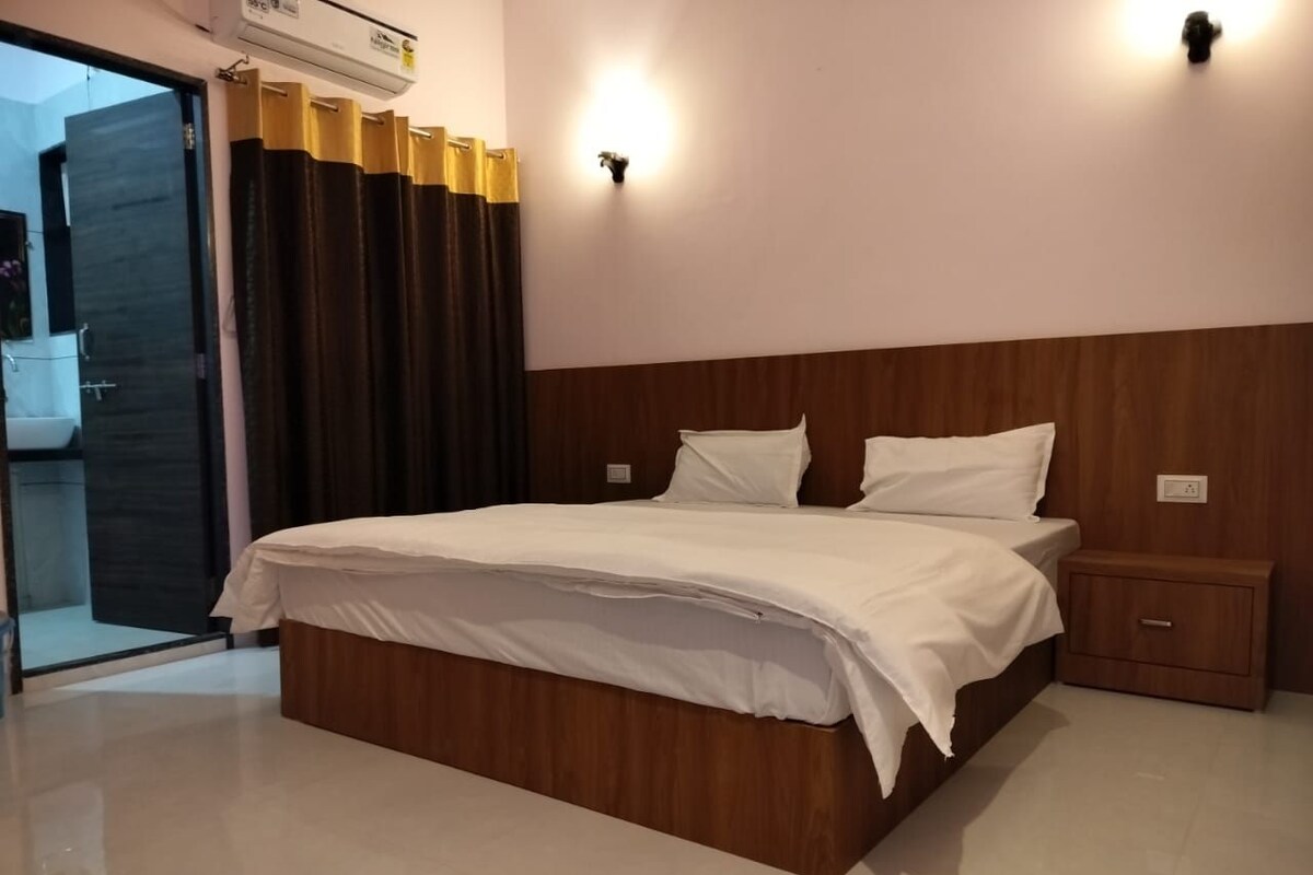 A bedroom with a wooden bed frame, white bedding, a nightstand, and a wall-mounted light fixture.