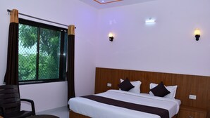 A bedroom with a large bed, a wooden headboard, two bedside tables, a small round table, a chair, and a window with curtains.