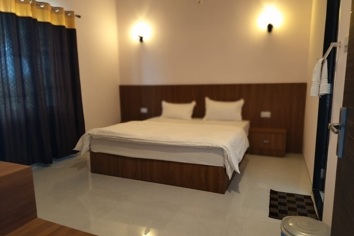 Une chambre d’hôtel avec un lit, deux tables de chevet, une tête de lit en bois, une petite table, une poubelle bleue et un tapis noir sur le sol.