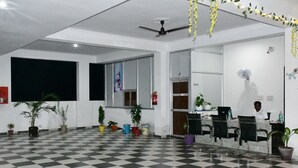 A hotel lobby with a checkered floor, potted plants, a reception desk, and a ceiling fan.