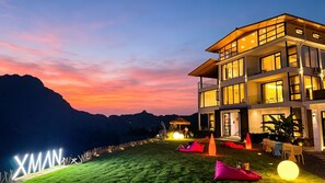 Un hotel de varios pisos con diseño moderno, amplios ventanales y un área exterior bien iluminada con asientos.