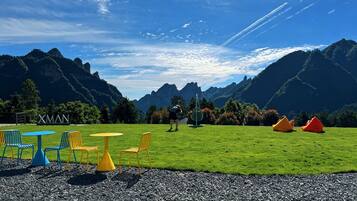 Un espace extérieur verdoyant, avec des tables et des chaises, une pancarte indiquant « XMAN » et un paysage montagneux en arrière-plan.