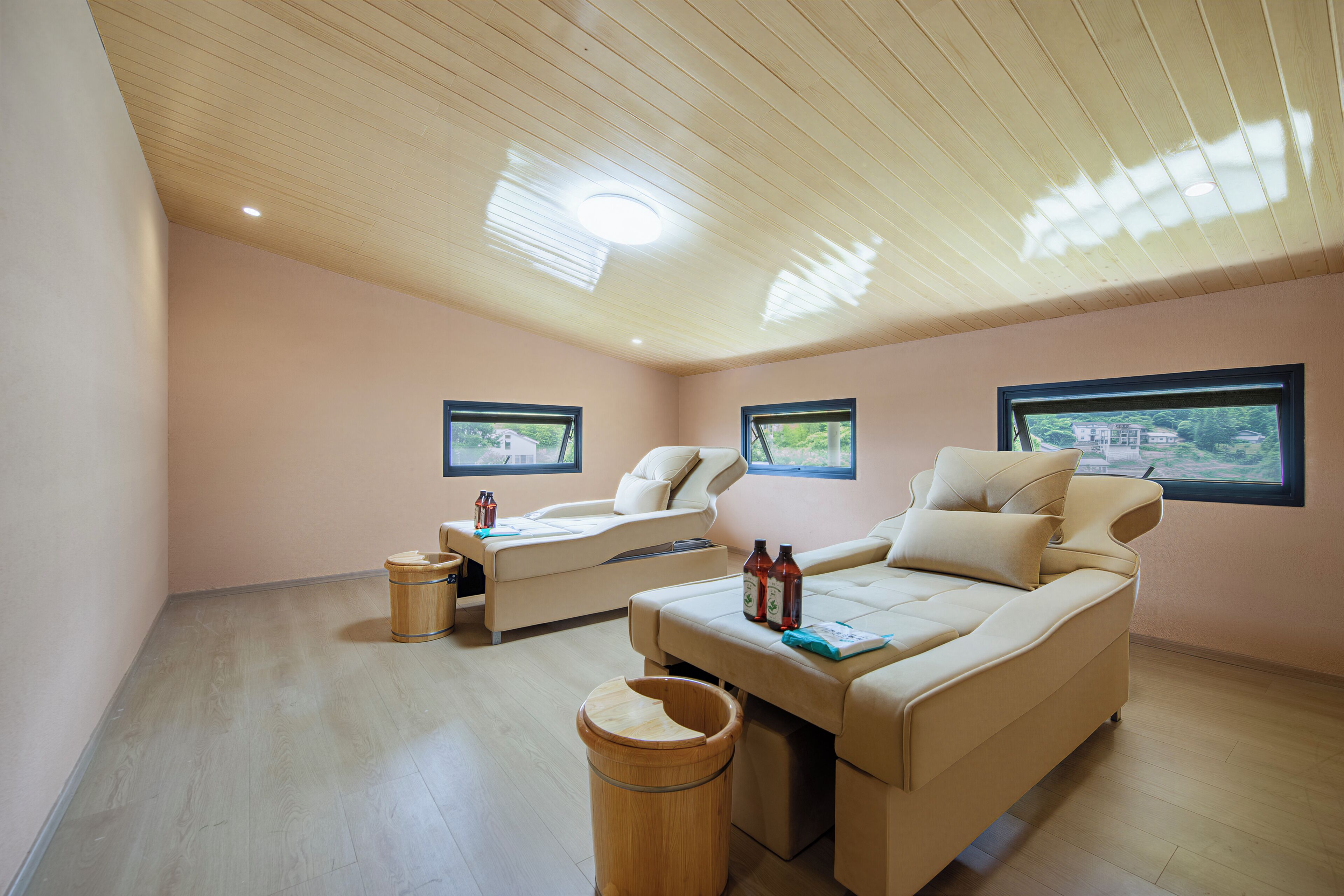 Une salle de spa équipée de deux tables de massage, dotée d’un plancher en bois et de grandes fenêtres offrant une vue dégagée.