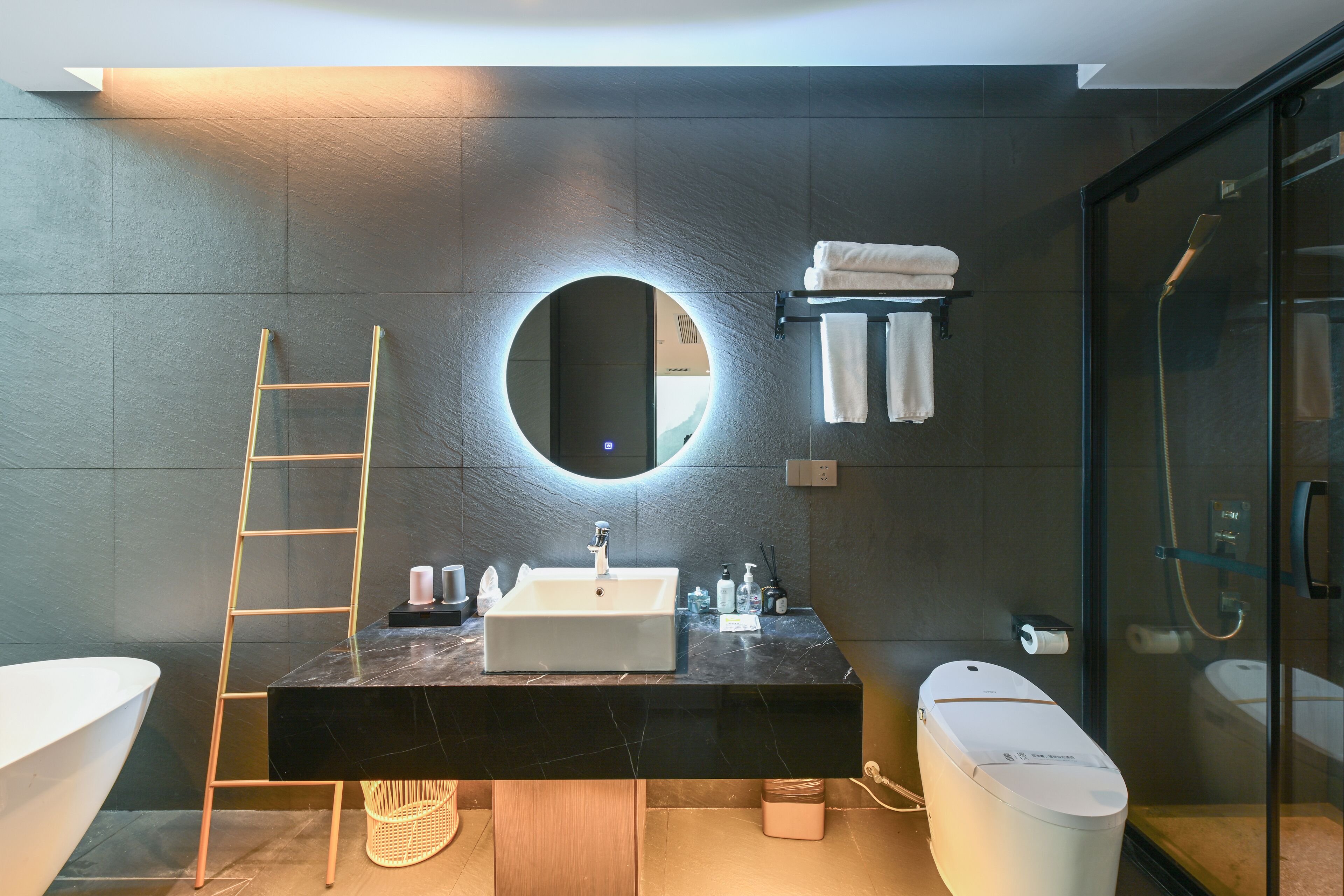 A modern bathroom with a large mirror, a white sink, a glass shower enclosure, and a wooden ladder.