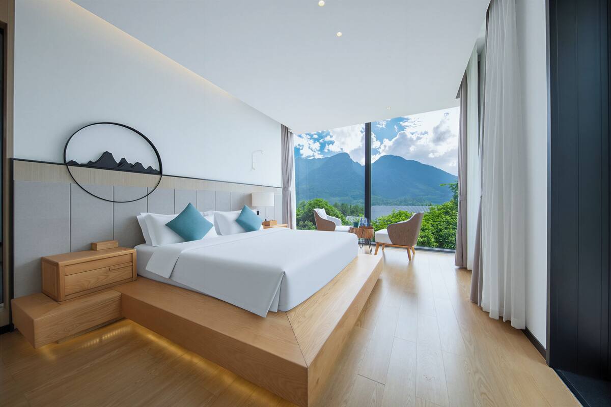 Une chambre moderne avec un lit, des tables de chevet et une vue sur les montagnes grâce à de grandes fenêtres.