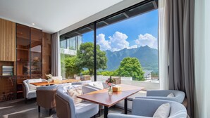 A modern living room with a large window, a wooden bookshelf, and a dining area. - XMAN Sunrise Peaks Resort (Zhangjiajie)