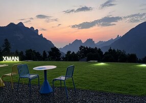 A patio with two chairs and a table, a neon sign, and a view of mountains.
