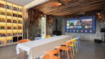 A conference room with a long table, colorful chairs, a bookshelf, and a large screen displaying various images.