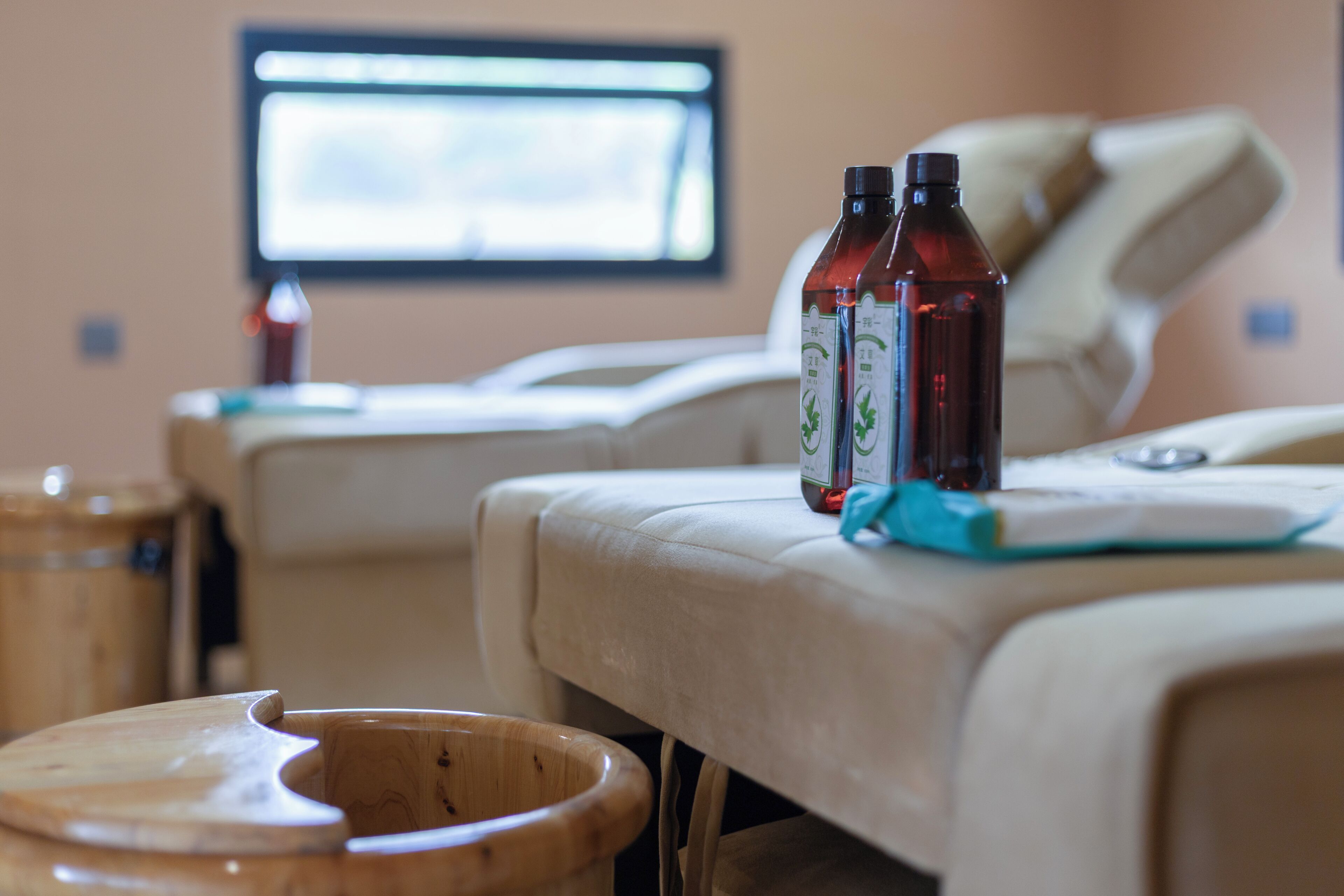 A massage therapy room with a massage table, wooden foot bath, and two bottles of oil on the table.