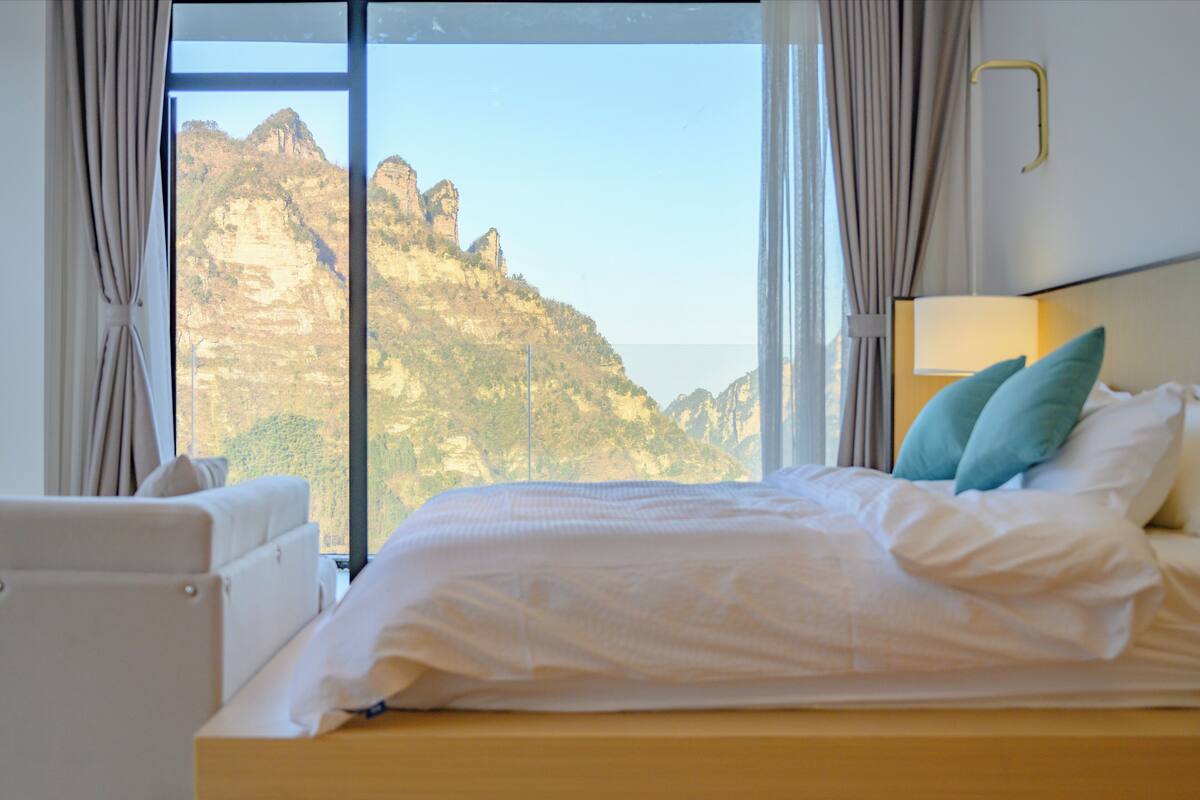 Une chambre d’hôtel avec un lit, une vue sur un paysage montagneux et une fenêtre avec des rideaux.