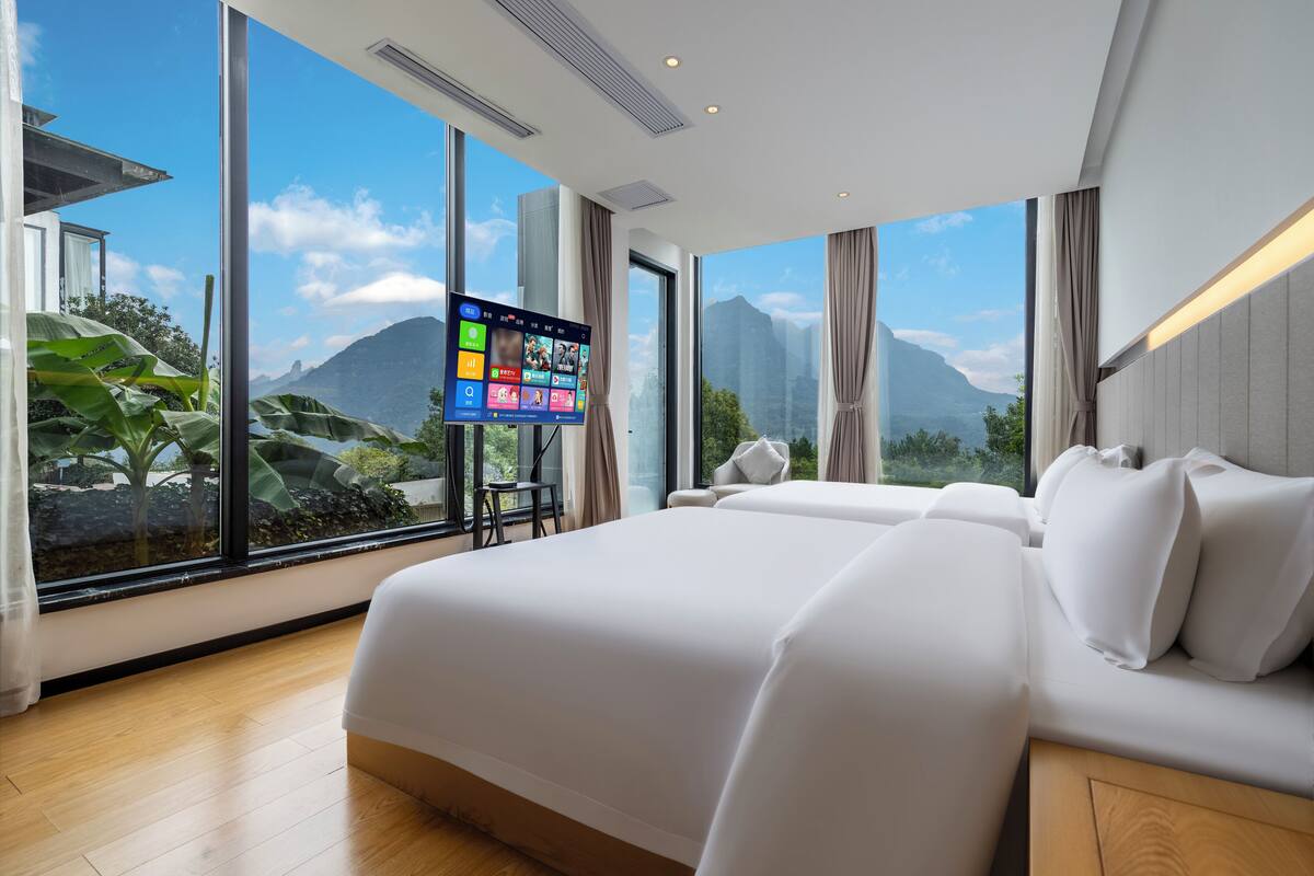 Une chambre d’hôtel moderne dotée d’un grand lit, d’un téléviseur à écran plat et offrant une vue sur les montagnes grâce à de grandes fenêtres.