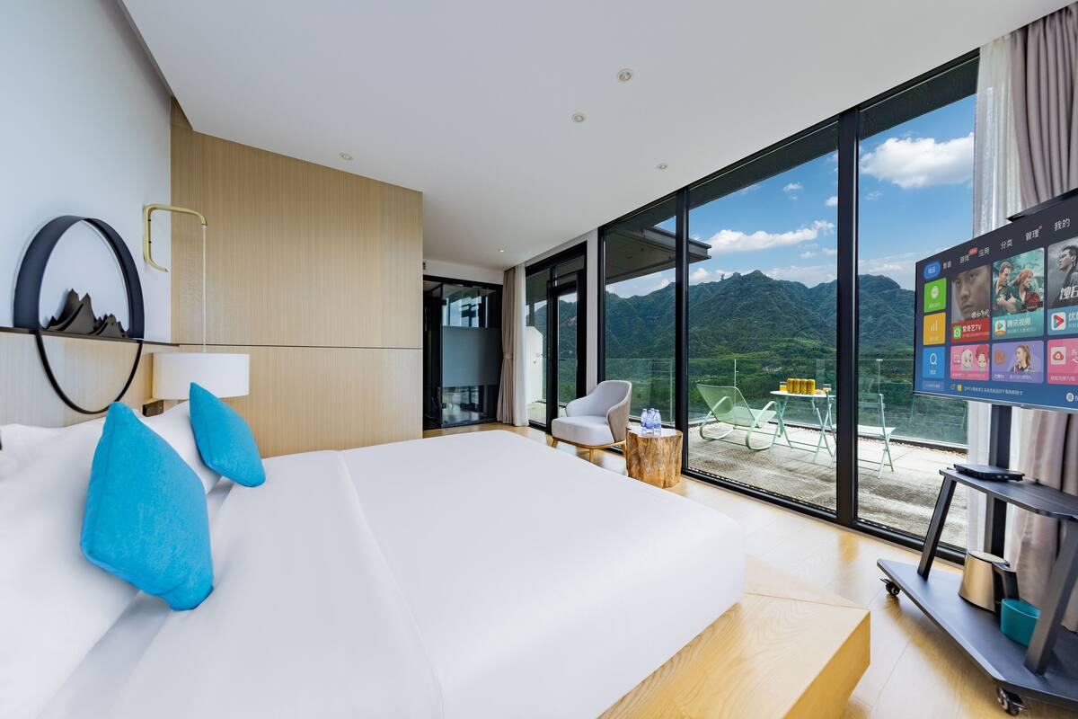 Une chambre d’hôtel moderne dotée d’un grand lit, d’une télévision, d’un balcon avec une table et des chaises, et offrant une vue sur la montagne.