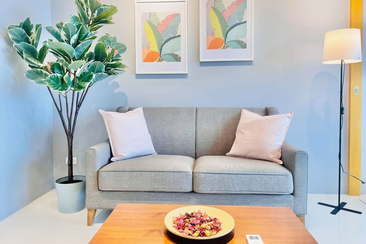 A modern living room with a grey sofa, two framed abstract art pieces, a potted plant, and a wooden coffee table with a bowl of dried flowers.