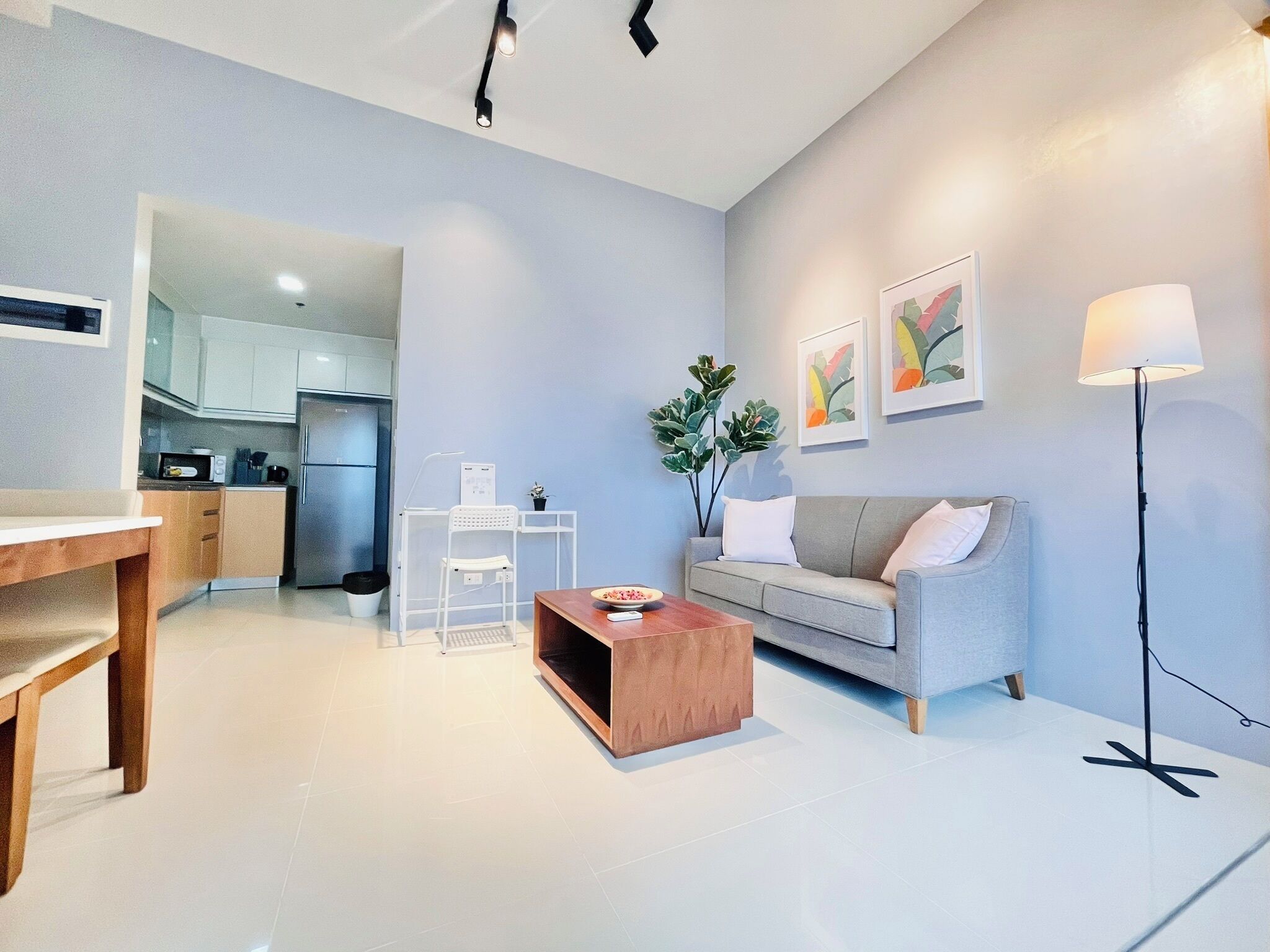 Ein modernes Wohnzimmer mit einem grauen Sofa, einem Holztisch und einer Stehlampe. Im Hintergrund ist eine Küchenzeile erkennbar.