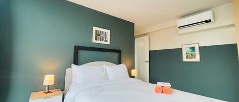 A neatly made bed in a hotel room with teal walls, a white headboard, and two bedside tables with lamps.