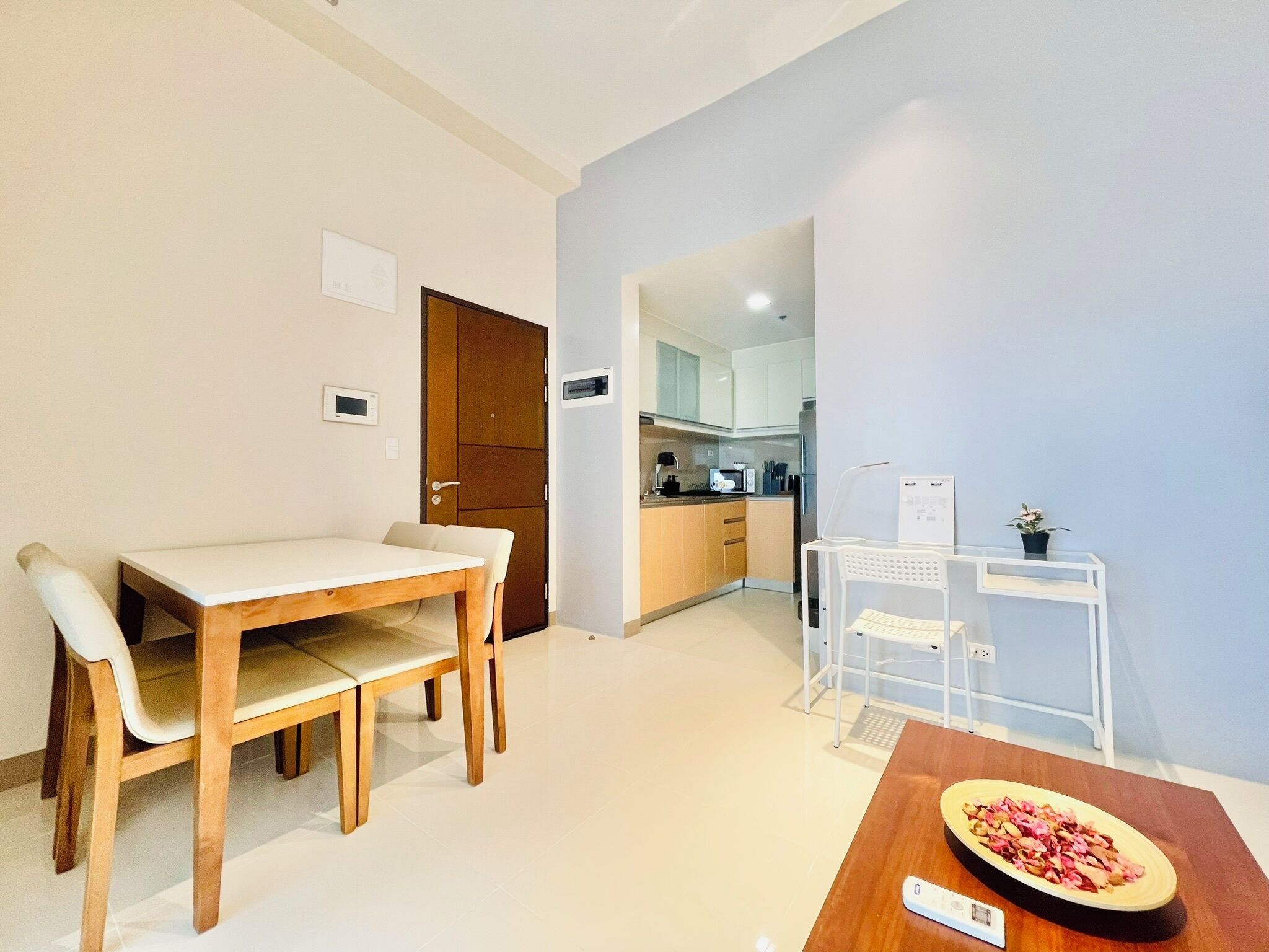 A modern kitchen with white cabinets, a wooden dining table with chairs, and a small white desk with a computer.
