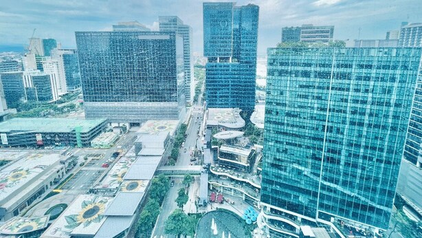 A high-rise urban area with modern glass buildings, a central roundabout, and surrounding greenery. - One Uptown Residence Near St Lukes (Taguig)