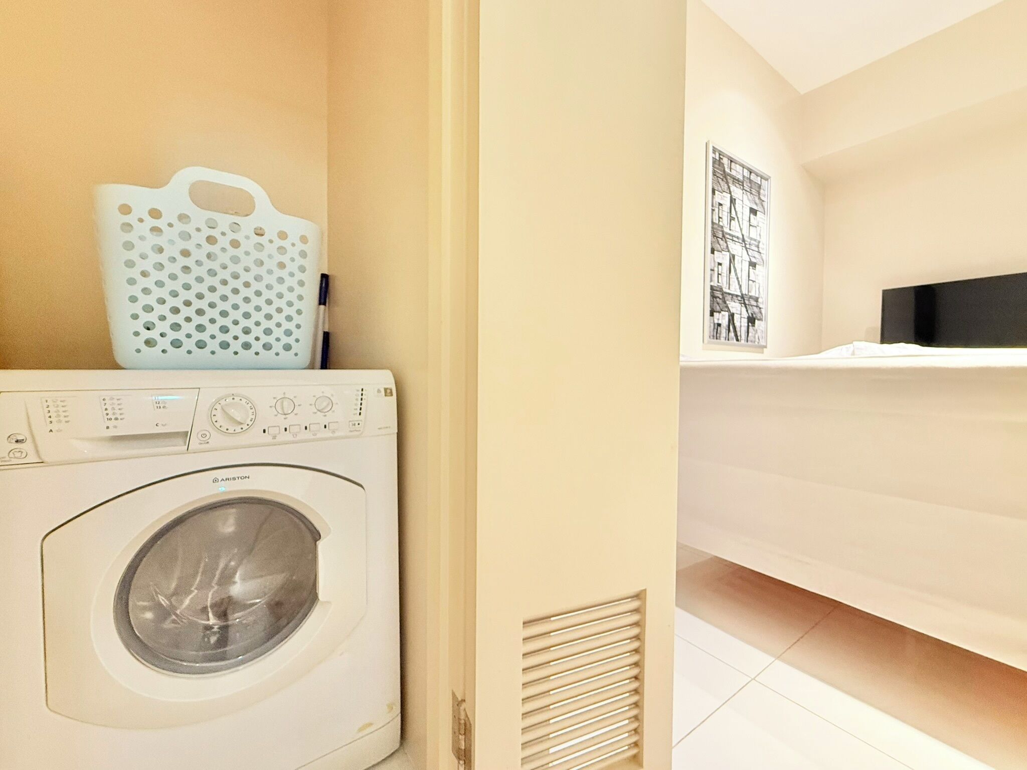 A laundry room with a front-loading washing machine, a drying rack, and a wall-mounted television.