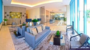 A modern lobby with a grey sofa, a reception desk, and a large window. - One Uptown Residence Near St Lukes (Taguig)