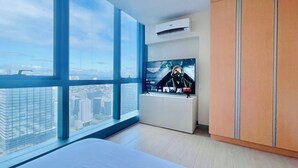 A modern hotel room with large windows, a flat-screen TV, and a wardrobe. - One Uptown Residence Near St Lukes (Taguig)