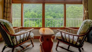 A room with a large window offering a view of a forested area. There are two wooden chairs with cushioned seats and backs. - Goshikionsen Goshikinoyu ryokan (Takayama)