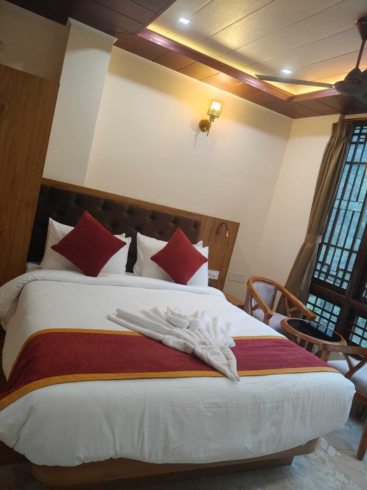 A neatly made bed with a red and white bedspread, a wooden headboard, and a red throw blanket. There is a wooden chair and a small table beside the bed.