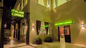 An Italian Corner and Russian Corner restaurant with illuminated signs, outdoor seating, and a reflective glass facade. - Nubia real estate aqua beach (Hurghada)