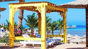 A yellow gazebo with white lounge chairs, palm trees, and a view of the ocean. - Nubia real estate aqua beach (Hurghada)