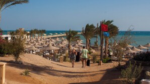 A beach resort with rows of thatched umbrellas, palm trees, and a clear view of the sea. - Nubia real estate aqua beach (Hurghada)