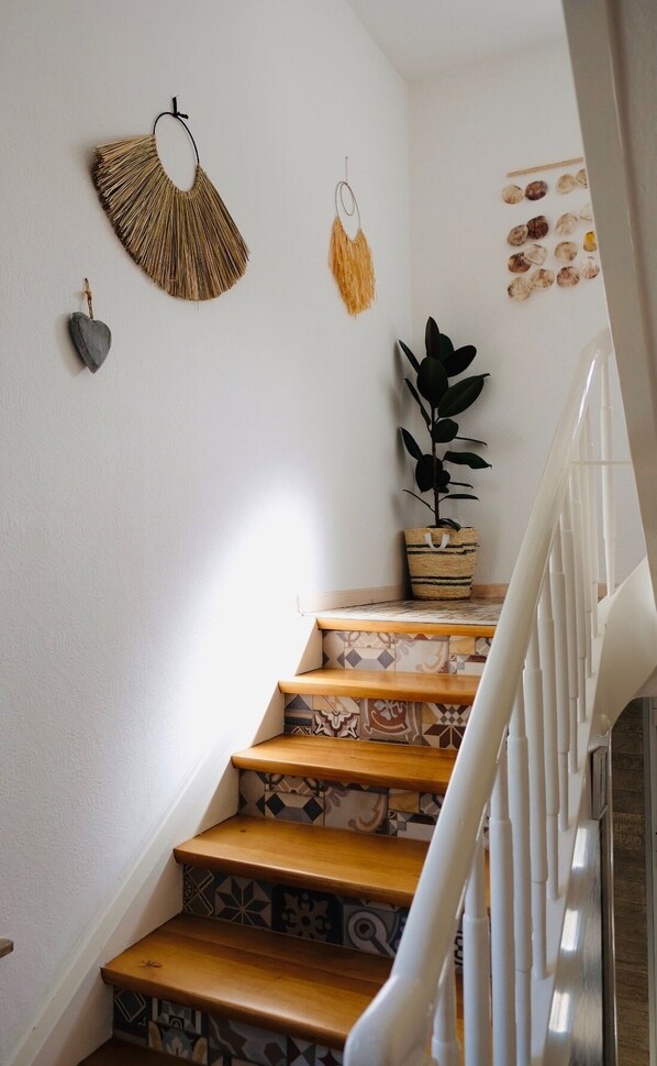 A staircase with patterned tiles, a potted plant, and wall decorations including a heart-shaped object and two hanging items. - Hacienda Rooms (Friedrichshafen)