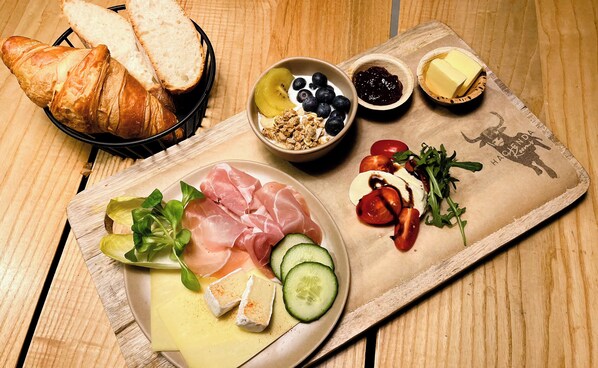 Ett träbord med ett urval av matvaror, inklusive bröd, ost, charkuterier, grönsaker och frukt.