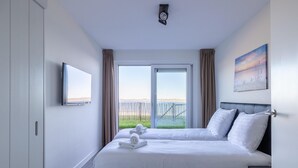 A hotel room with a large bed, a television, a painting, and a view of the beach. - Apartment in Sint-Annaland near Marina (Sint-Annaland)