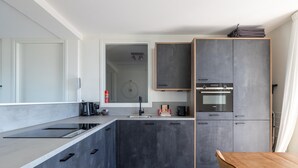 A modern kitchen with a large island, dark cabinets, and a wooden dining table. - Apartment in Sint-Annaland near Marina (Sint-Annaland)