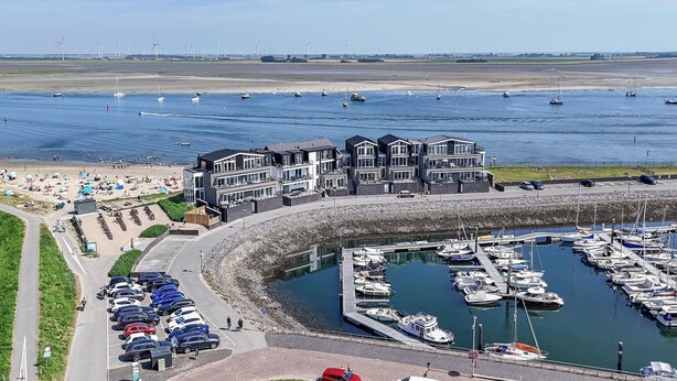 A marina with boats docked, a parking area, and a beach with people.