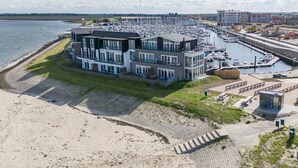 Un hotel frente al mar con varios pisos, un puerto deportivo con barcos y una zona de playa.