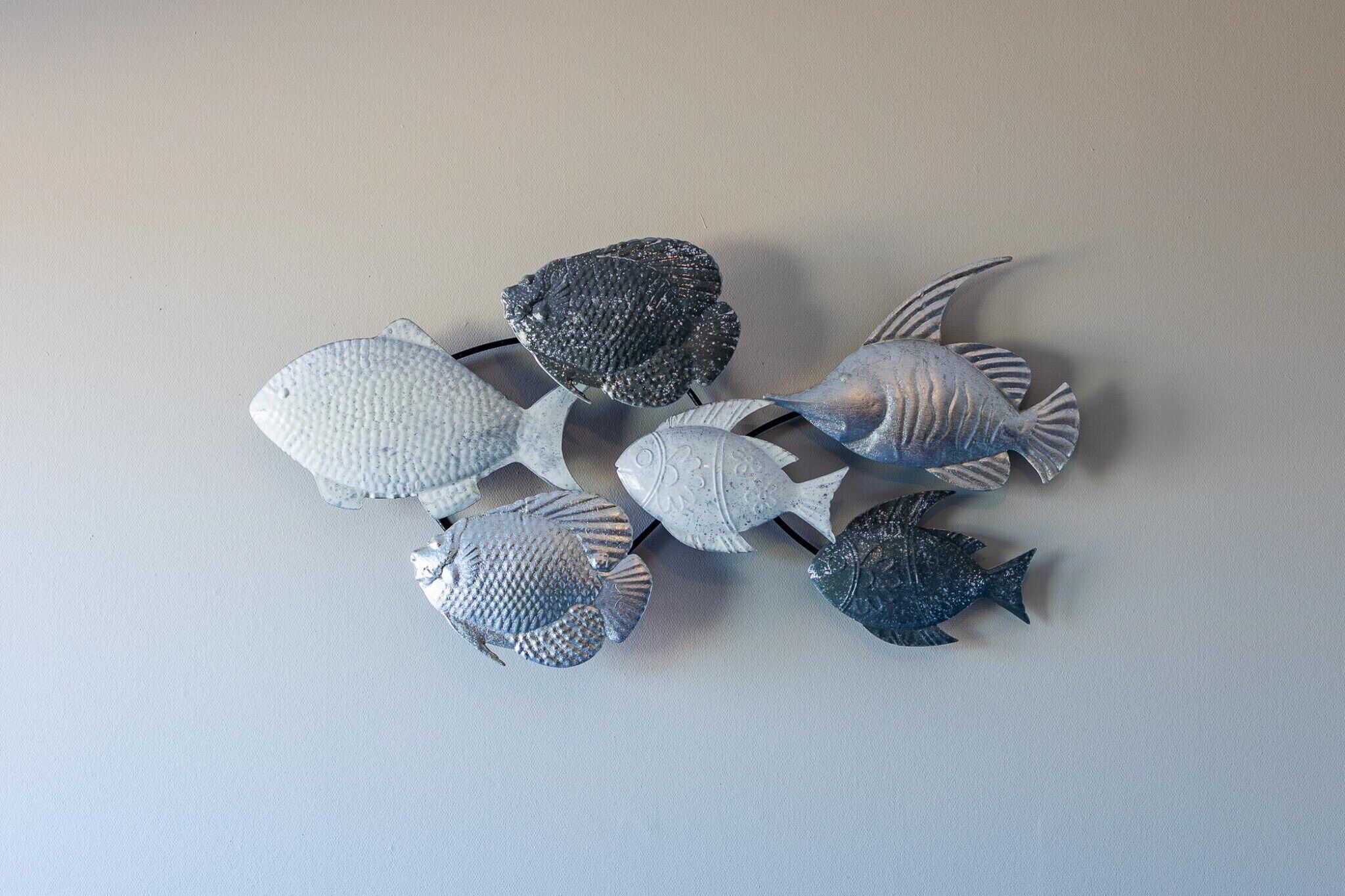 A collection of metallic fish sculptures on a plain wall.