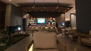 Una sala de estar moderna con sofá, sillas, televisor y una zona de bar con estanterías y plantas.