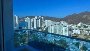 Un edificio alto con varios pisos, un balcón y vistas de un paisaje urbano con montañas al fondo.