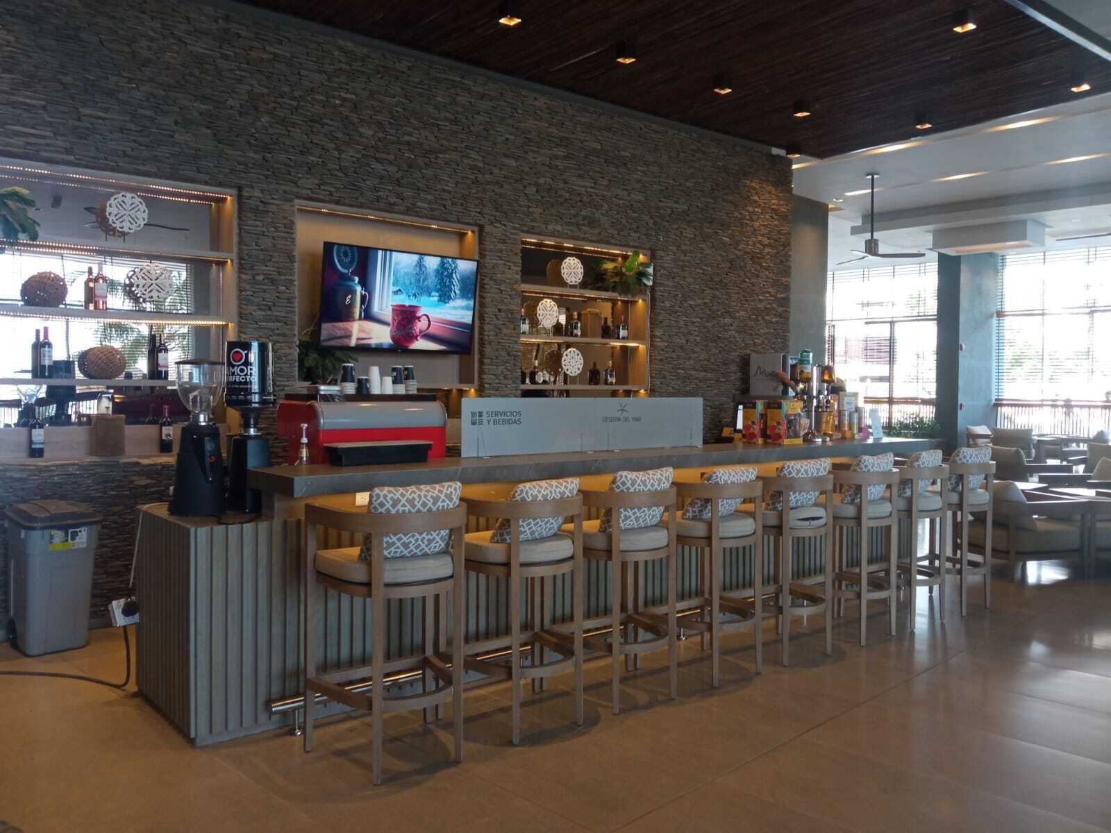 A modern bar area with a stone wall, bar stools, a television, and shelves with bottles.