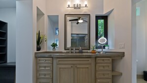 A bathroom with a large vanity, a ceiling fan, a mirror with lights, and a window with a view of trees. - Casa Famlee - Duplex House(sleeps 8) with Pool & Hot Tub in Cabo San Lucas! (Cabo Bello)