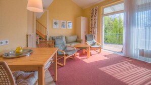 Un salon chaleureux avec une table en bois, des chaises, un canapé et un balcon offrant une vue sur la verdure.