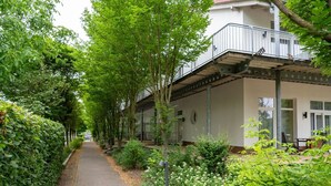 A pathway lined with lush greenery and white flowers, leading to a building with a balcony and a covered outdoor area. - Elegant eingerichtete Ferienwohnung (Granzow)